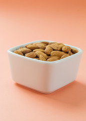 Almonds nuts in white bowl on coral pink background