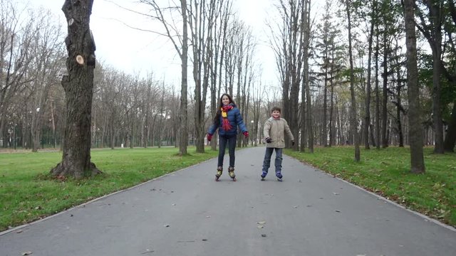 Boy and girl ride in autumn park on rollers