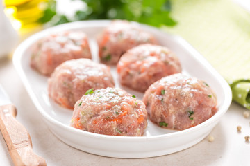 Raw meatballs on white plate, cooking in kitchen