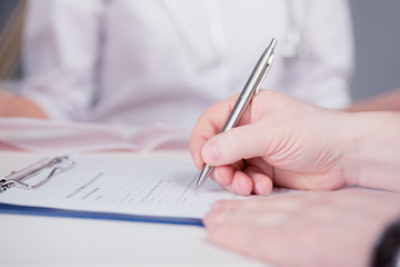 Naklejka premium The patient completes the questionnaire in a doctor's office. Pen in hand. The image depth of field.