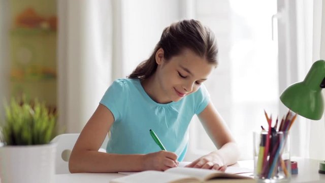 happy girl with book writing to notebook at home