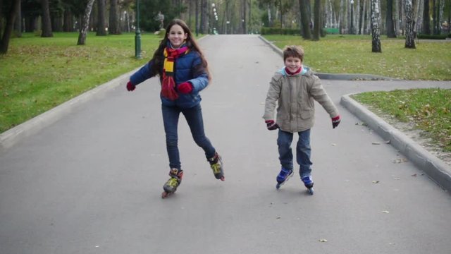 Boy and girl ride together in autumn park on rollers