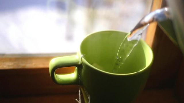 pour hot water in a cup standing near the window, to brew delicious tea, steam swirls, HD, 1920x1080.