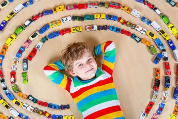 Cute little blond kid boy playing with lots of toy cars indoor.