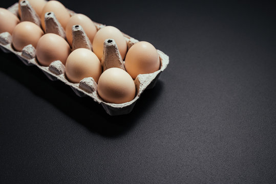 Cardboard egg box on black wooden background. Copy space. Eggs container.