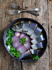 Delicious salted herring with red onion, salt and pepper on the old wooden background. Rustic style.