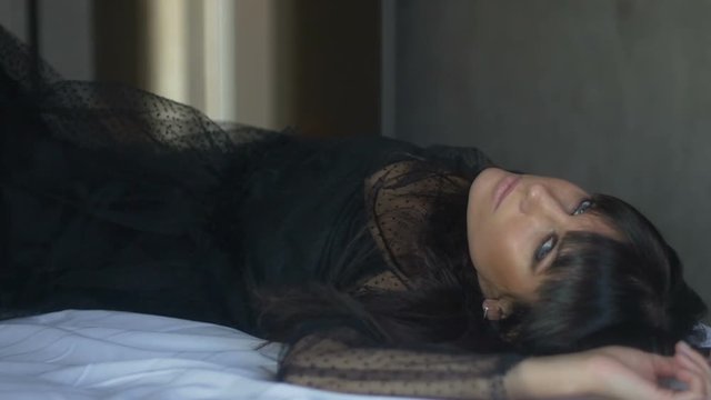 Brunette woman in black lies on bed and poses