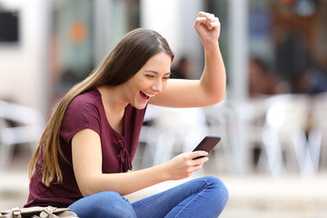 Excited woman with a phone in the street