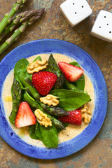 Fresh strawberry, green asparagus, baby spinach and walnut salad served on plate, photographed overhead on slate with natural light