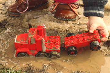 A child playing with a red car in the mud puddle.