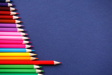 one red pencil standing out from the series of colorful pencils. On blue background.