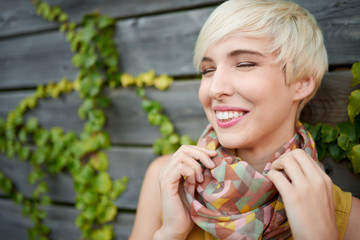 Beautiful short haired platinum blond woman standing against an ivy fence backdrop