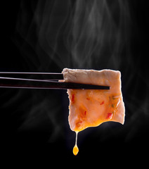 Sukiyaki or Shabu shabu pork slice with sauce in chopsticks and smoke