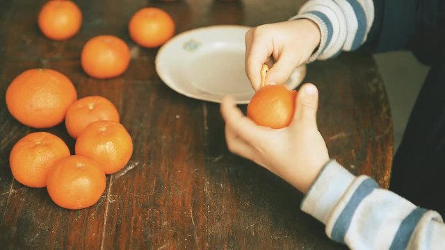 boy cleans tangerine. Tangerines lie on a wooden table.