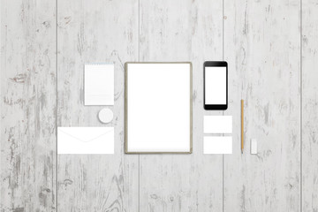 Clean paper, pad, envelope, badge, business card and mobile phone screen for design presentation. Top view of white wooden desk.