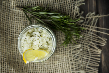 jar of homemade scrub on sacking on a wooden table. It made of salt, sugar, olive oil, lemon juice, lemon peel and rosemary