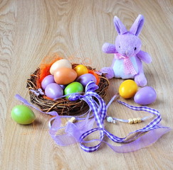 Easter eggs in a nest with  decorative ribbons and easter rabbit on wooden background.