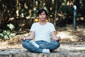 young black man wearing white shirt sitting in the park exercising yoga