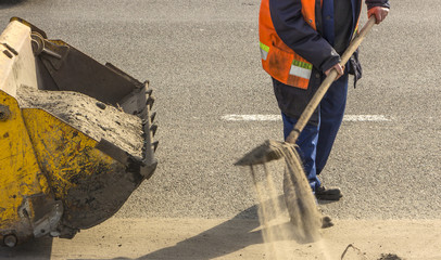 Road worker cleans the road from the sand