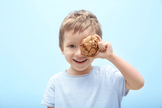 Cute little boy holding cookie on light background