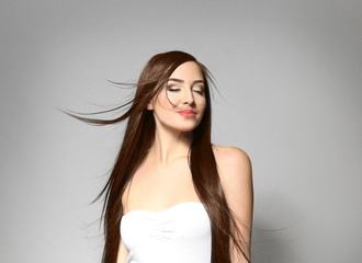 Beautiful young woman with long straight hair on light background