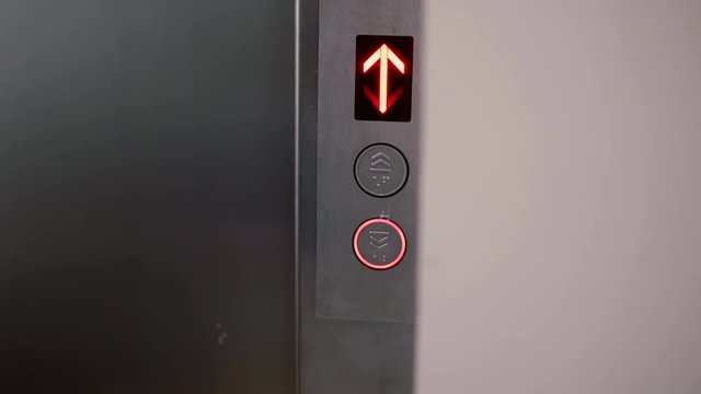 Woman comes to elevator. Female hand presses the elevator button and it light to go down. Girl is waiting. 4K