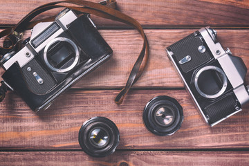 Old film cameras with lenses and strap on wooden background. Vintage toned and top view