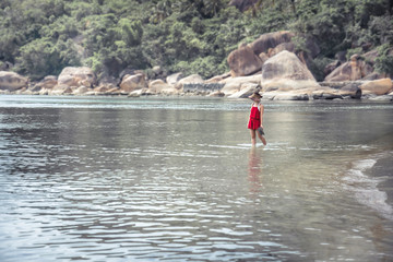 Lonely woman in red dress on tropical beach in the sea during vacation