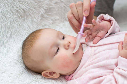 Female Hand Giving Baby Medicine Spoon. The Child Allergy, Rash On The Cheeks