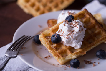 Belgian waffles on white plate, napkin and rustic background.