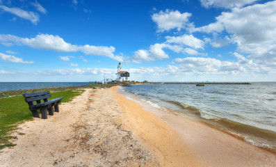 Banc seul sur la plage sur fond de phare sur la côte de la mer et ciel bleu avec nuages au coucher du soleil au printemps aux Pays-Bas. Paysage avec sable jaune, mer et balise. Nature. Rivage