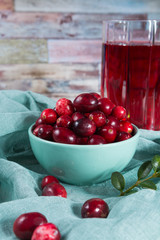 Red cranberry juice in a glass, cranberries in the green clay bowl on the table