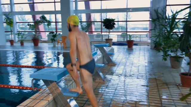 Muscular swimmer warming up, rises on the bedside table and jumps into the pool and swim a distance for a while. Competition.