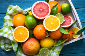 Citrus fruit in wooden tray on blue table.