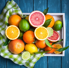 Citrus fruit in wooden tray on blue table.