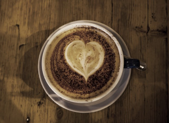 cup of coffee with heart shape in it. made out of froth, wooden top