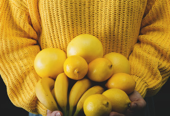 Young woman in yellow sweater holds a bunch of yellow fruit. Selective focus and small depth of field.