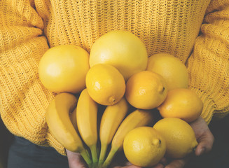 Young woman in yellow sweater holds a bunch of yellow fruit. Selective focus and small depth of field.