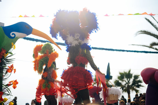 Blurry silhouette of unrecognizable joyful dancing woman wearing carnival feathers costume on sunny street outdoors background. Back view