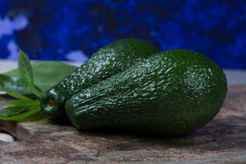 Green ripe avocado with leaves on granite plank