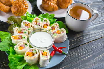 Pita rolls with lettuce, sauce, chili pepper, eclairs and tea