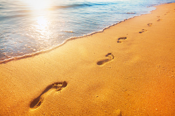 beach, wave and footprints at sunset time