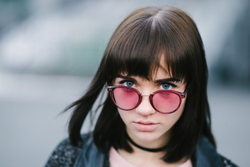 outdoor portrait of a young and very beautiful brunette with big blue eyes in a pink glasses on the blurred background