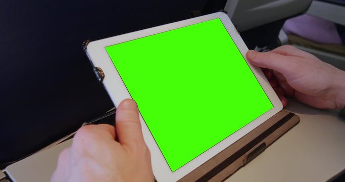An airplane passenger uses a green screen tablet PC at his seat. Green screen with optional tracking points for advanced screen replacement.  	