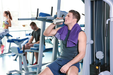 Fototapeta na wymiar Young handsome man drinking water in gym