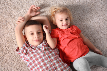 Cute little brother and sister lying on soft carpet