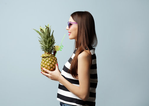 Young beautiful woman with cocktail in pineapple on light background