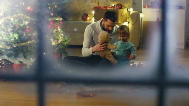 Looking Through Snowy Window. Sitting Under Christmas Three  Father and Daughter Play with Plush Bear. Shot on RED Cinema Camera 4K (UHD).