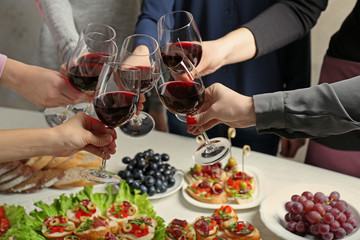 People clinking glasses with wine and delicious dishes on table