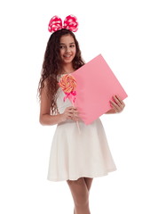 Lovely girl brunette with long hair in a white dress with a bow on her head with candy and a sheet...